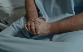 Person sitting on edge of hospital bed with their hands in their lab.